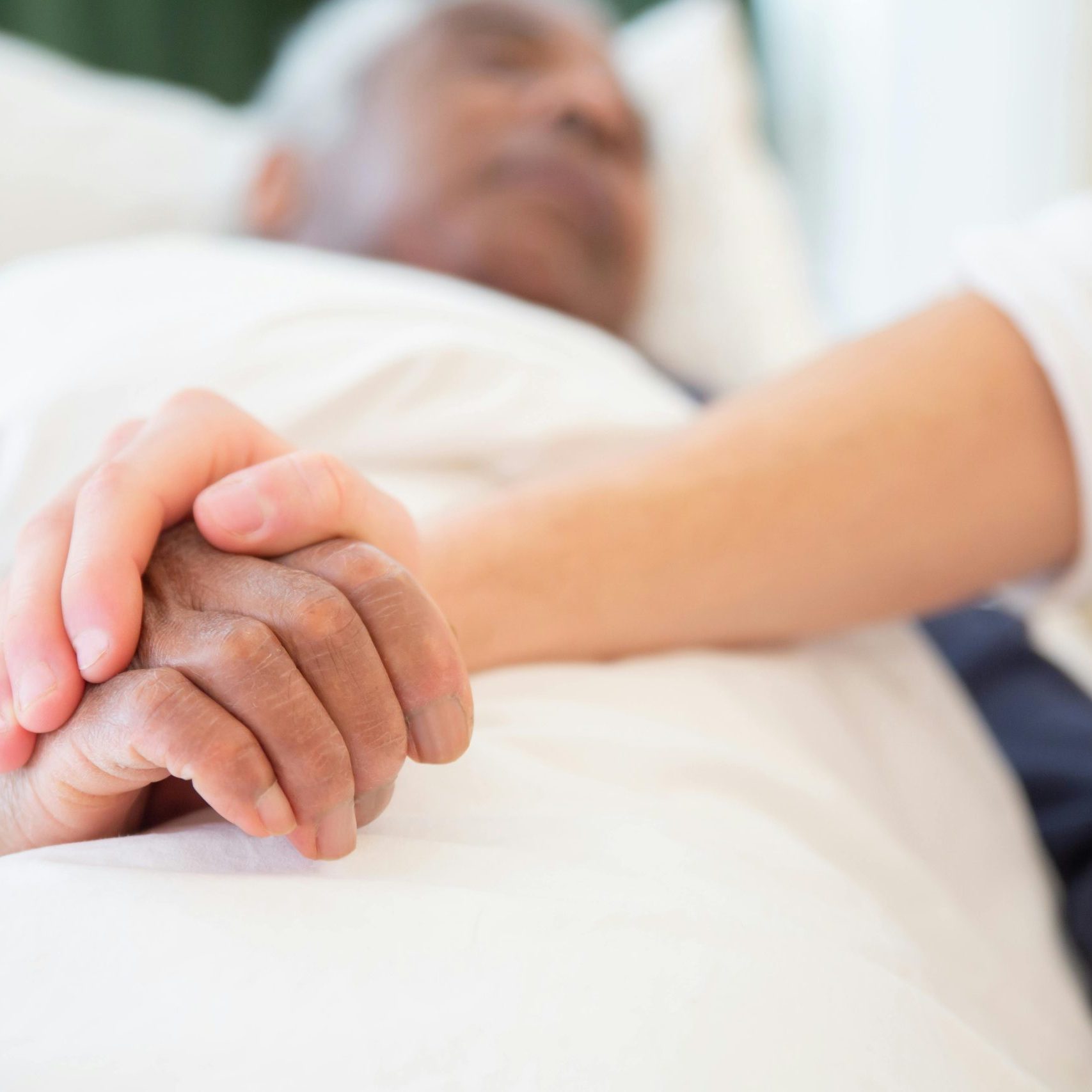 Frau hält einem älteren Mann in einem Krankenhausbett die Hand – © Kampus/Pexels